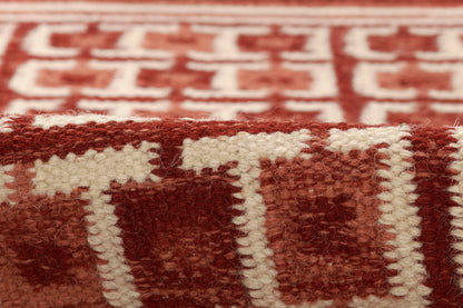 Close-up of a red and white woven rug with a geometric Nordic pattern and fluffy fringe.