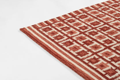Red and white Scandinavian-style rug with a diamond lattice pattern; flat-woven textile with a cropped corner visible.