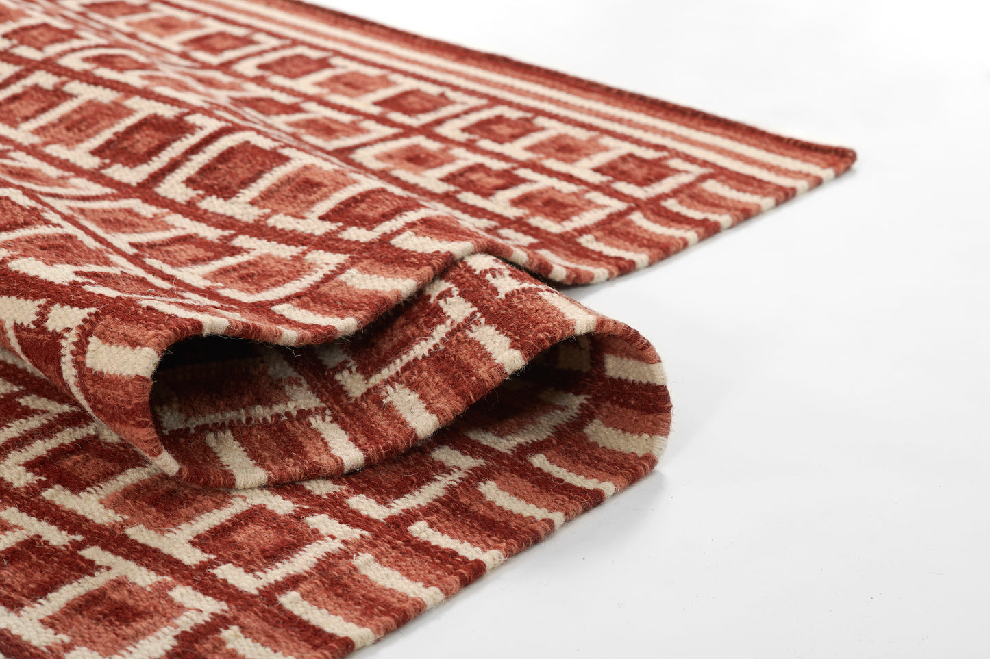 Red and white geometric-patterned Scandinavian rug, folded corner shows soft woven texture.
