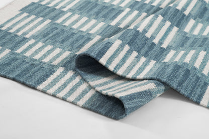 Blue and white Scandinavian-style woven rug with geometric striped pattern, folded edge.