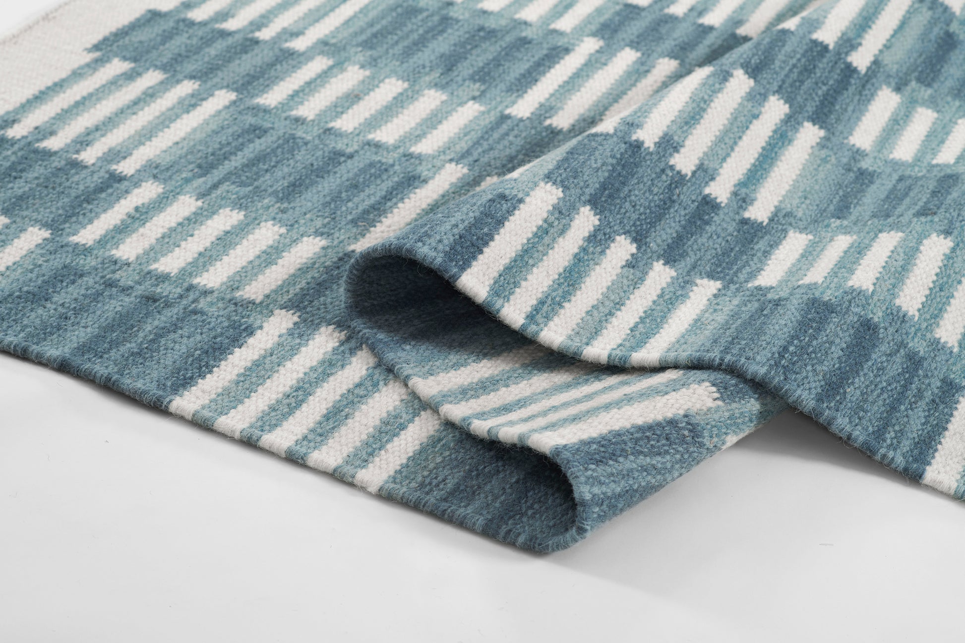 Blue and white striped Scandinavian-style rug with soft woven texture and folded edge.