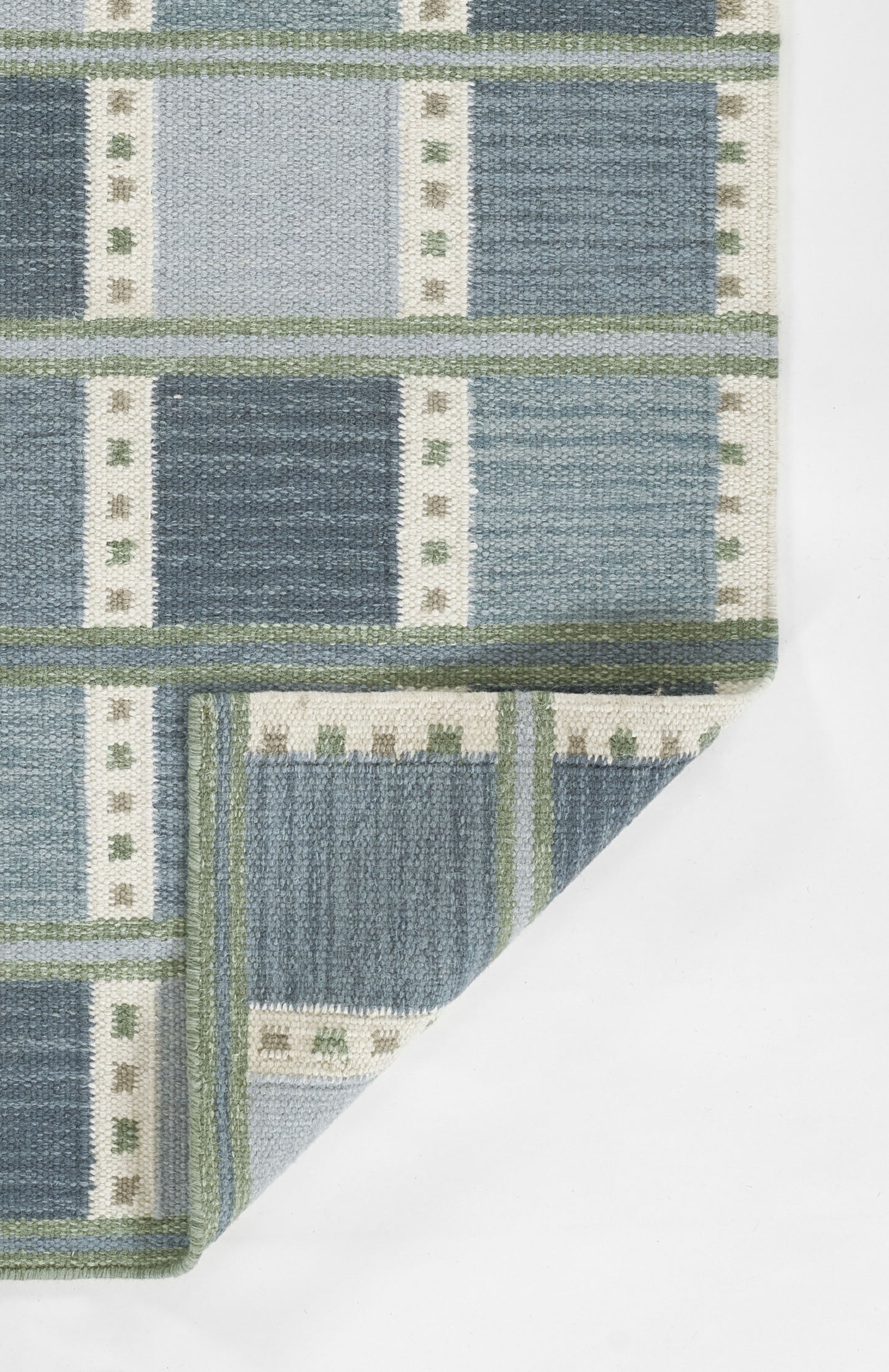 Scandinavian blue patterned rug with light and dark blue block panels, cream dotted borders, green trim; folded corner; 9' x 12'.