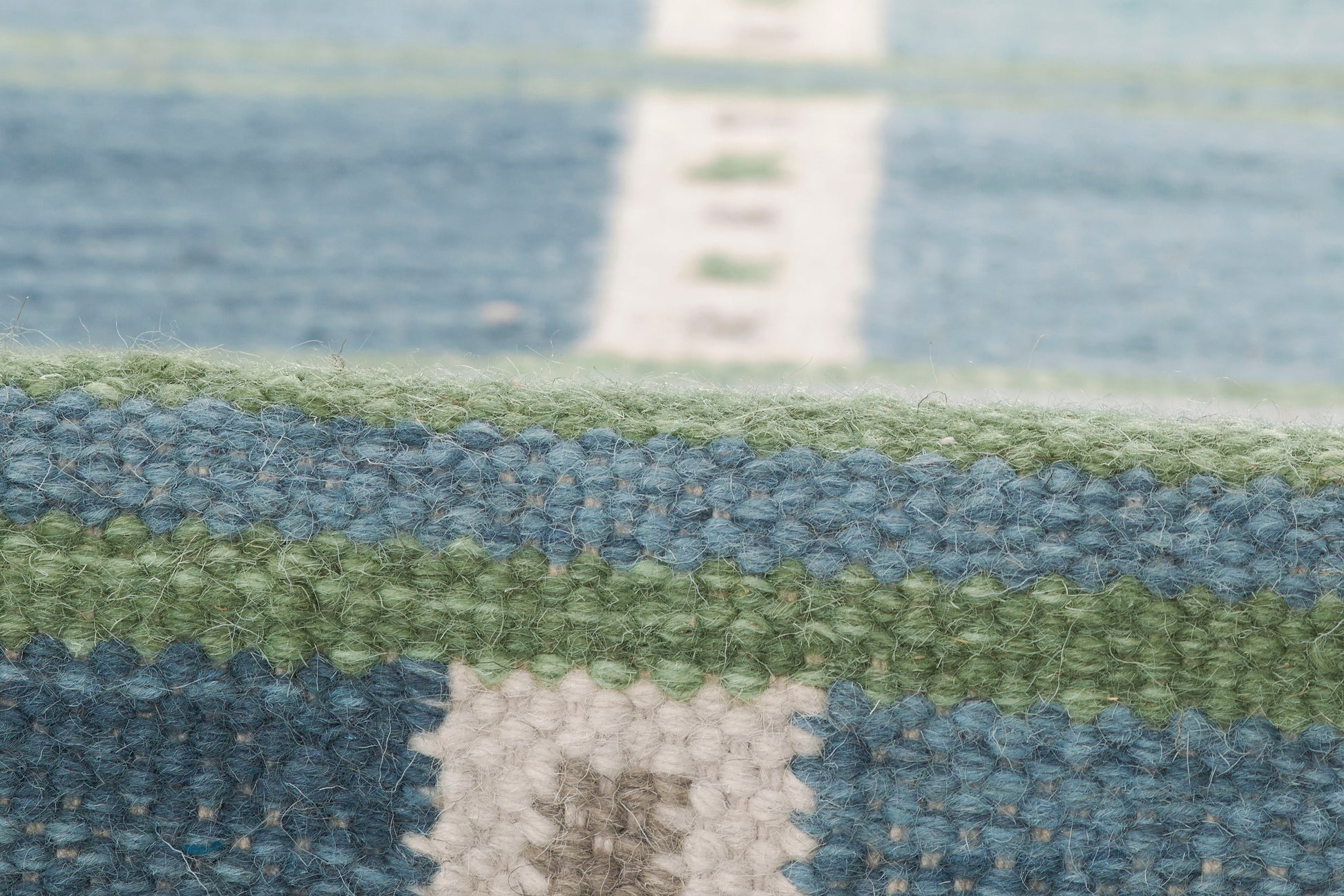 Close-up of a woven rug with blue, green & cream stripes; chunky textile with geometric pattern.