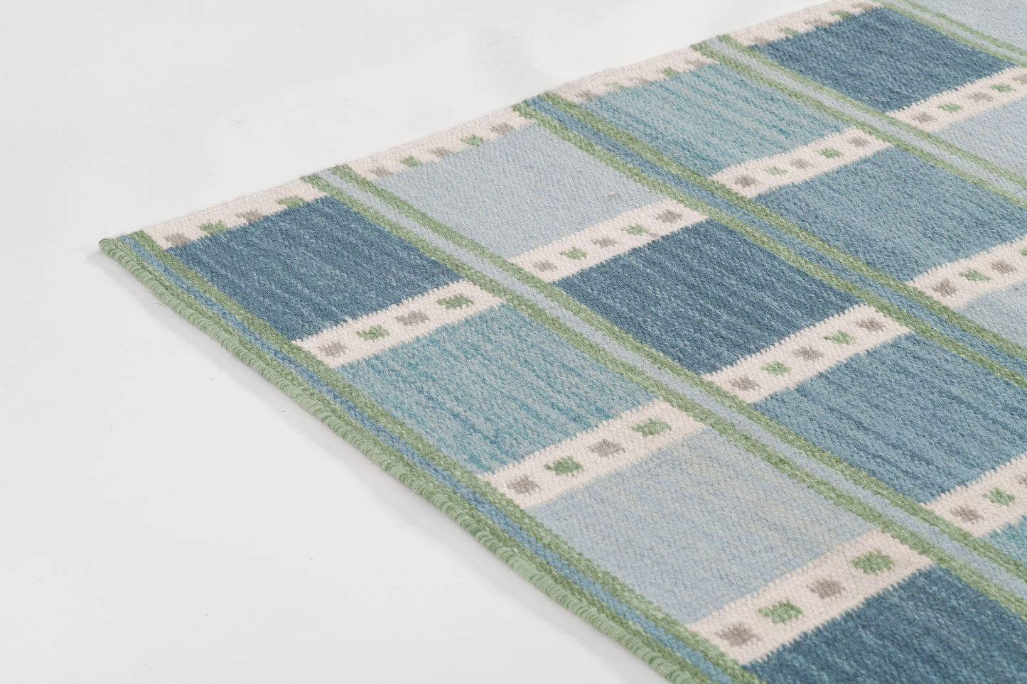 Scandinavian blue plaid rug, 9' x 12', with light and dark blues, white dotted stripes, green trim and fringe.
