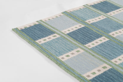 Scandinavian blue plaid rug, 9' x 12', with light and dark blues, white dotted stripes, green trim and fringe.