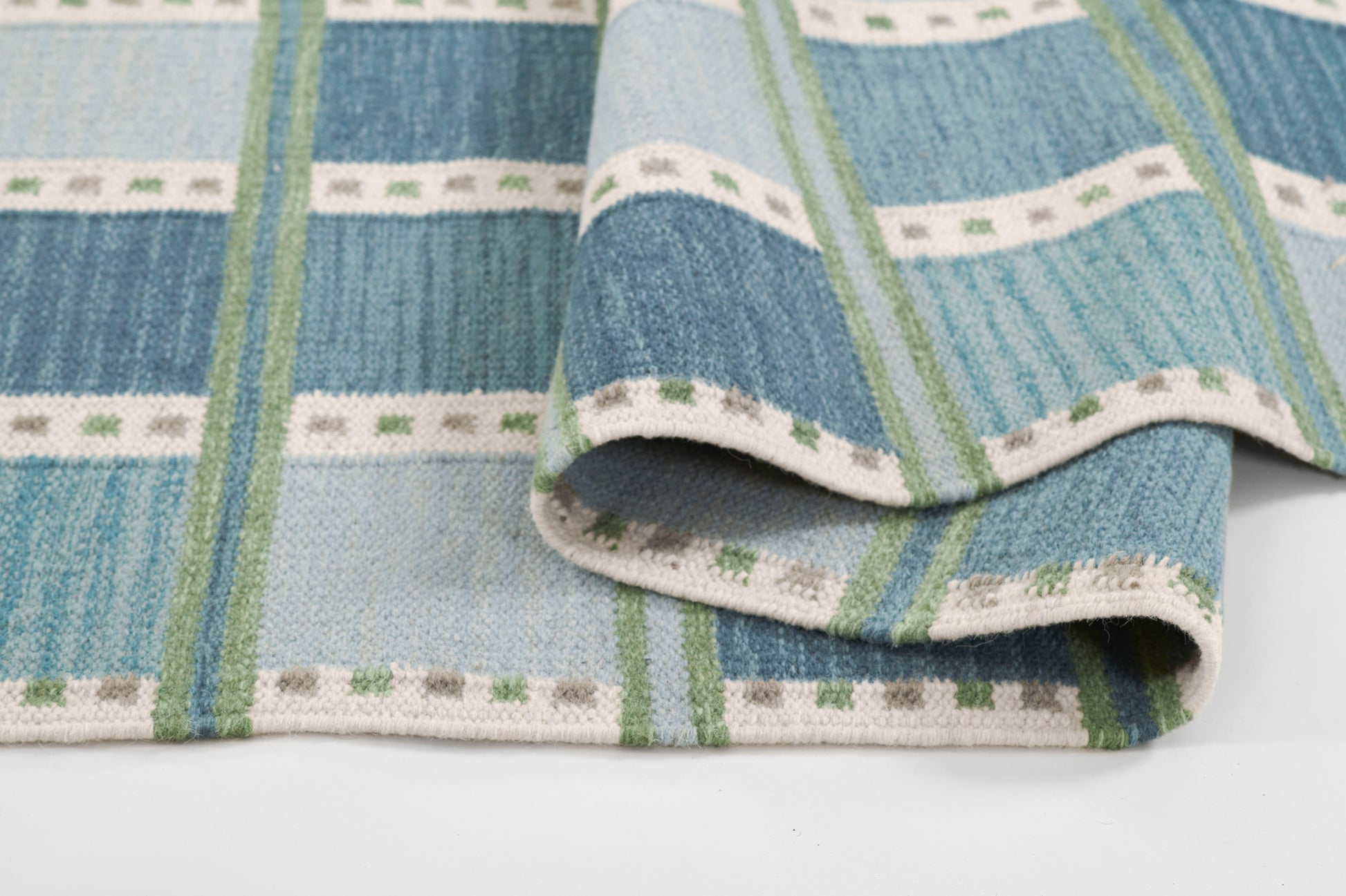 Blue striped woven rug with green accents and white dotted trim, folded, 9' x 12'.