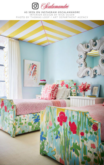 Bright pastel blue bedroom with floral upholstered chairs, pink bedding, yellow striped ceiling, and an ornate white mirror.
