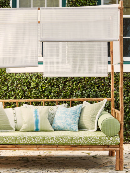 Wooden outdoor daybed with green botanical cushions, blue and cream pillows, and white shade panels on a bamboo frame.
