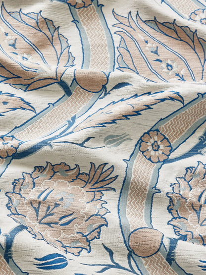 Cream decorative damask fabric with blue and peach floral motifs and a textured woven surface.