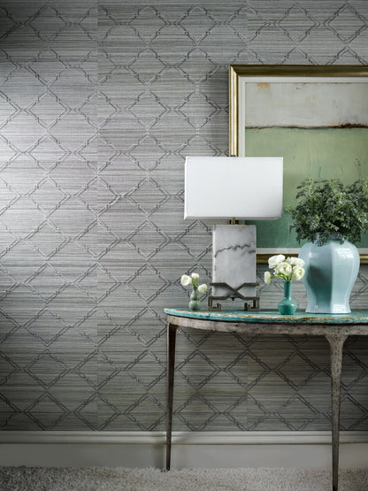 Side-table vignette with lamp on marble-base, turquoise vase, white flowers, and framed art on grey lattice wallpaper.