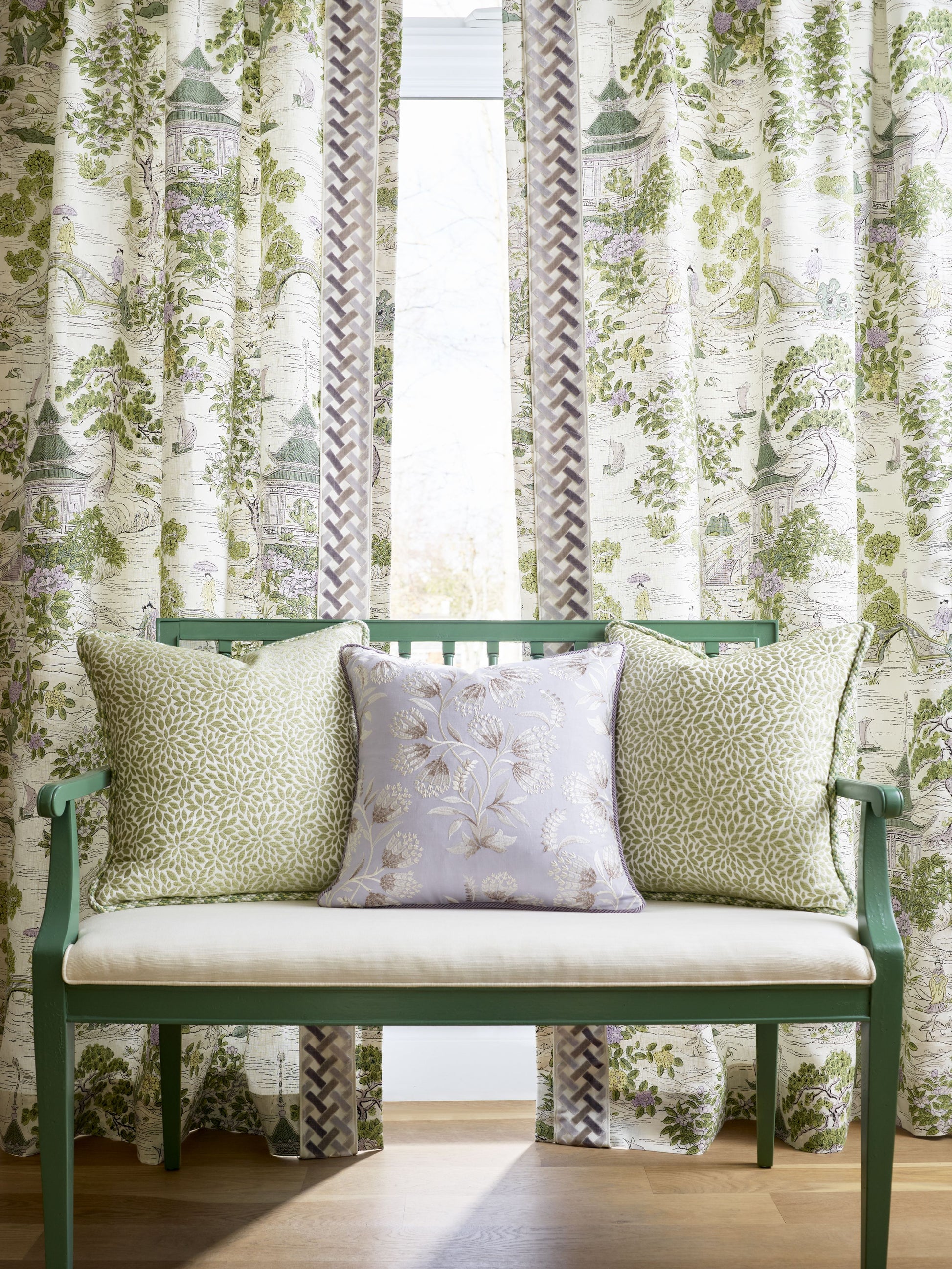 Green wooden bench with cream cushion and three botanical pillows; lavender center, greenery sides, lush curtains.