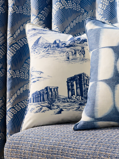 Blue and white cushions on a textured blue sofa; one shows ruins and camels, the other a blue geometric circle print.