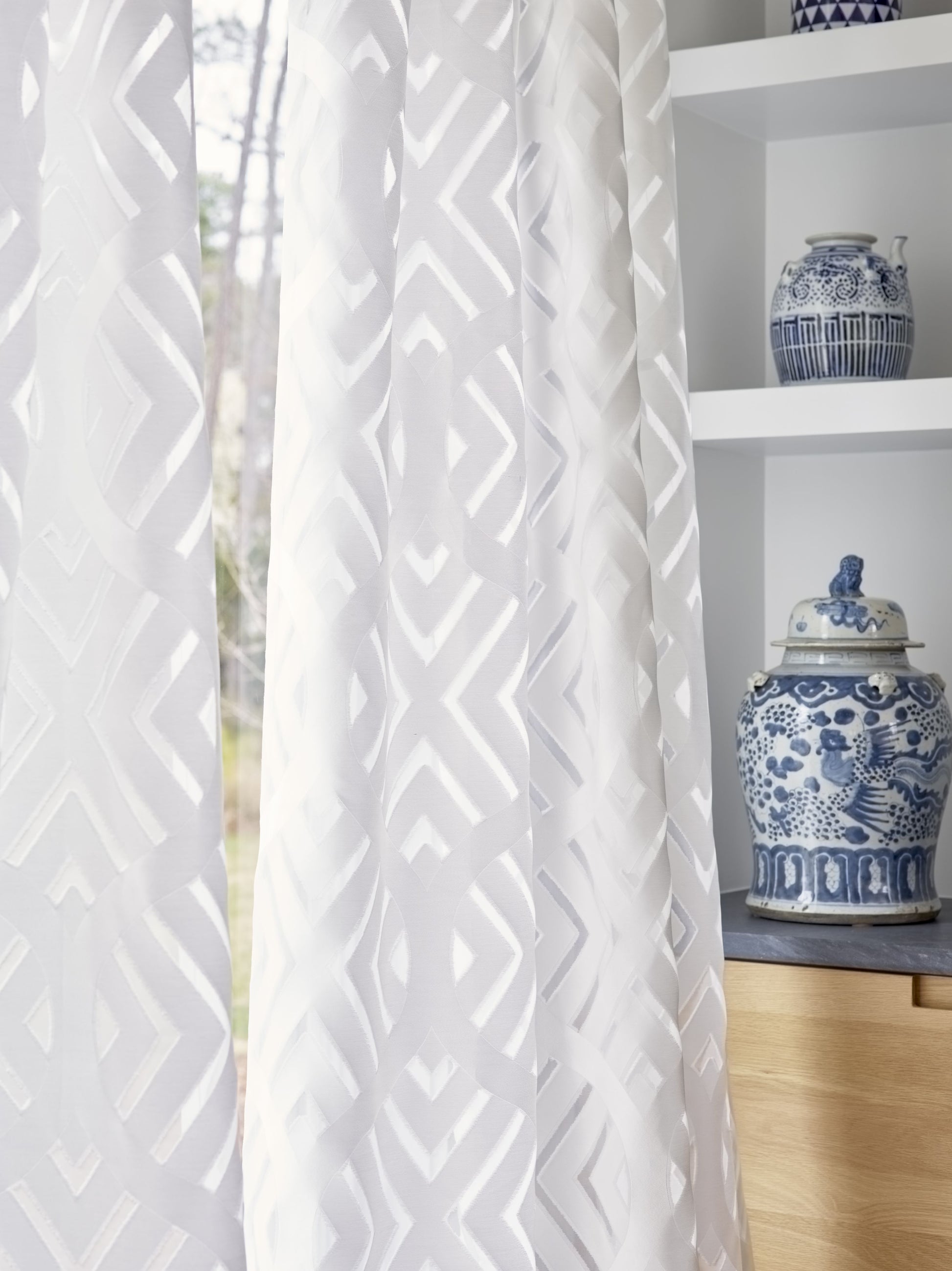 White textured curtain with embossed geometric pattern, draped by a window; blue-and-white ceramic jars on a shelf.