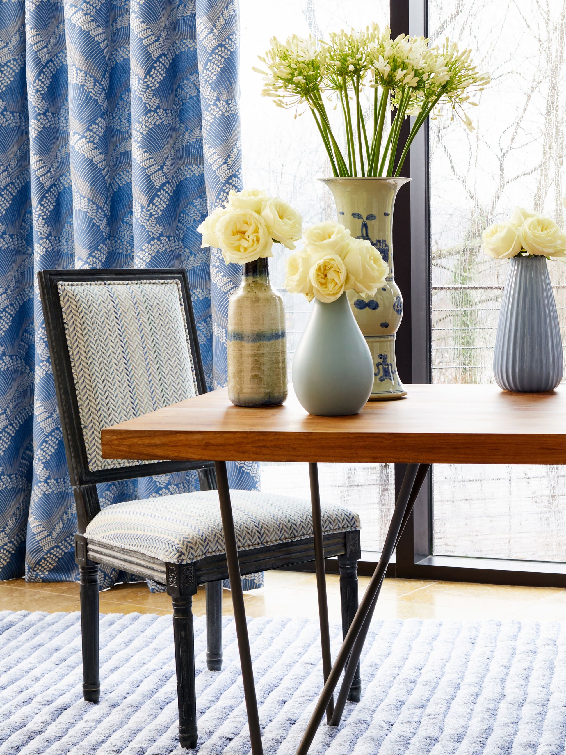 Arrow stripe fabric pattern; room scene with a wood table & black metal legs, blue patterned chair, cream flowers in vases, blue curtains & a bright window.