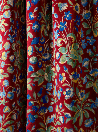 Close-up of red floral velvet fabric with blue, yellow and green blossoms and vines, velvet texture.
