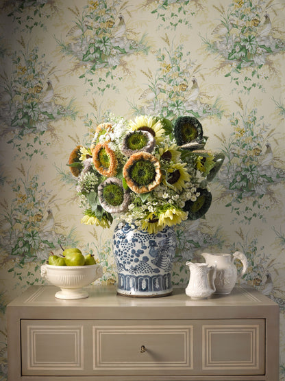 Sunflower bouquet in blue-and-white ceramic vase atop a beige dresser with floral wallpaper; bowl of apples nearby.