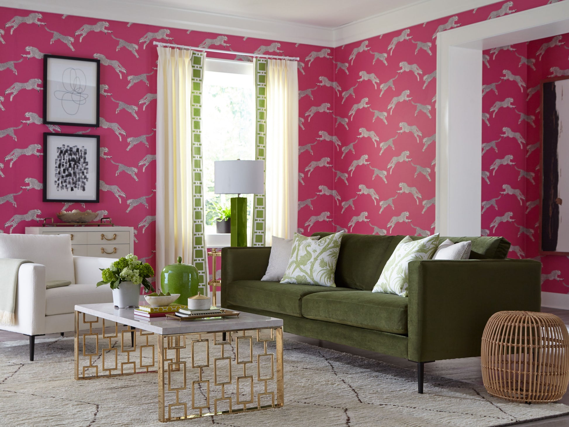 Bright pink wallpaper with white deer pattern, olive green sofa, white chair, gold geometric coffee table, wicker basket.