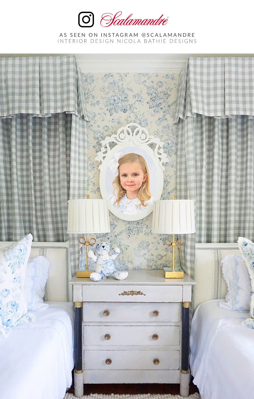 Pastel blue bedroom with distressed white nightstand, round ornate mirror, twin beds, gingham curtains, gold-base lamps.