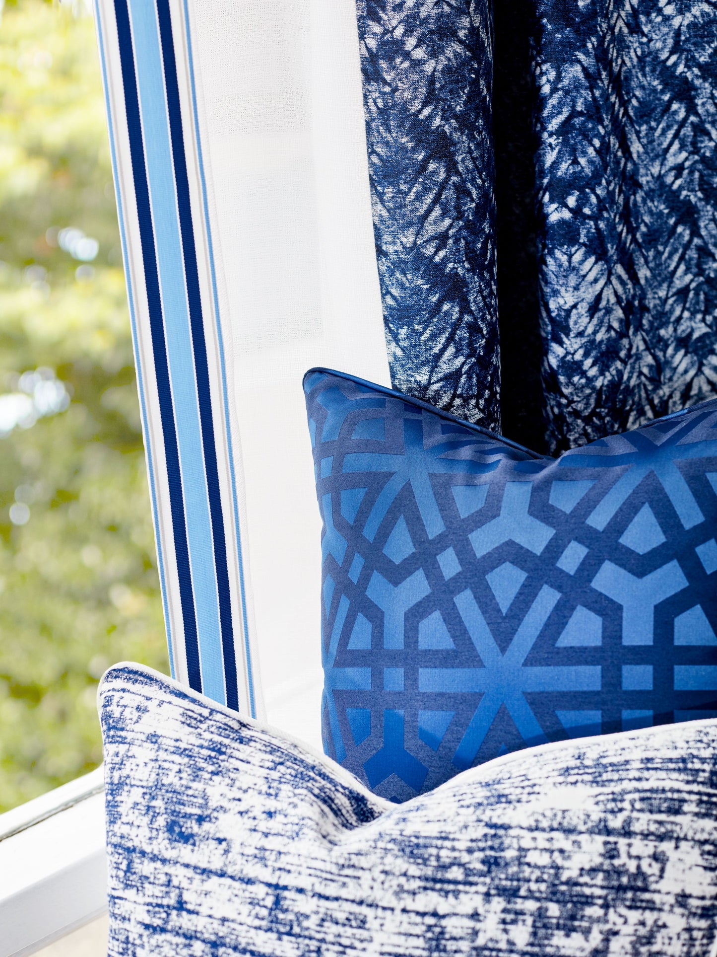 Blue geometric lattice pillow and blue textured cushion on a window seat with striped blue curtains.
