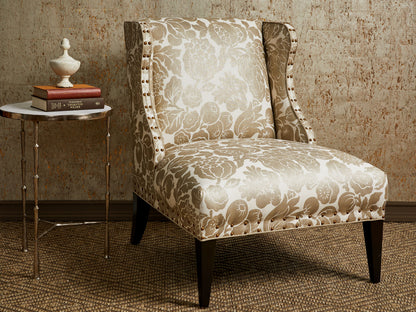 Beige damask upholstered wingback chair with nailhead trim and dark tapered legs beside a round marble-top side table with books and a white vase.