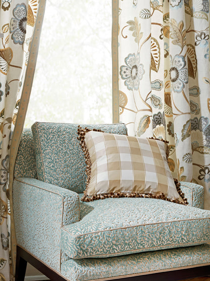 Teal patterned armchair with a beige check pillow and floral curtains in warm tones.