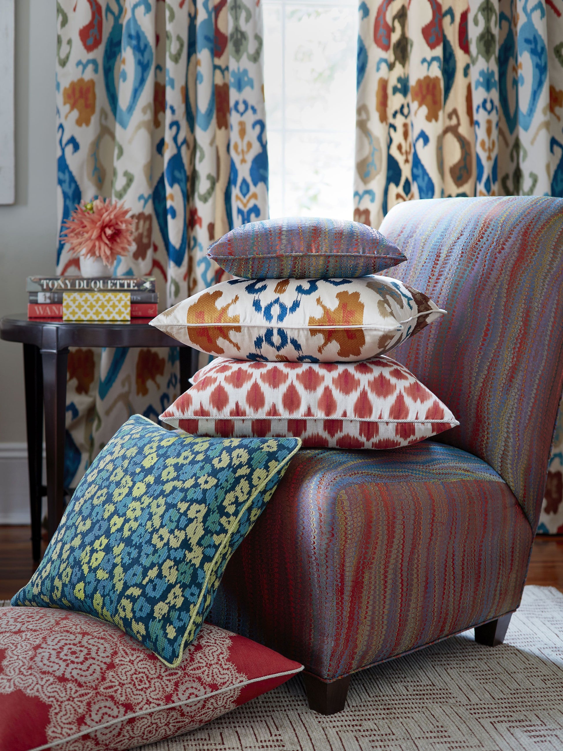 Stack of vibrant ikat-patterned cushions on a striped upholstered chair with bold curtains in the background.