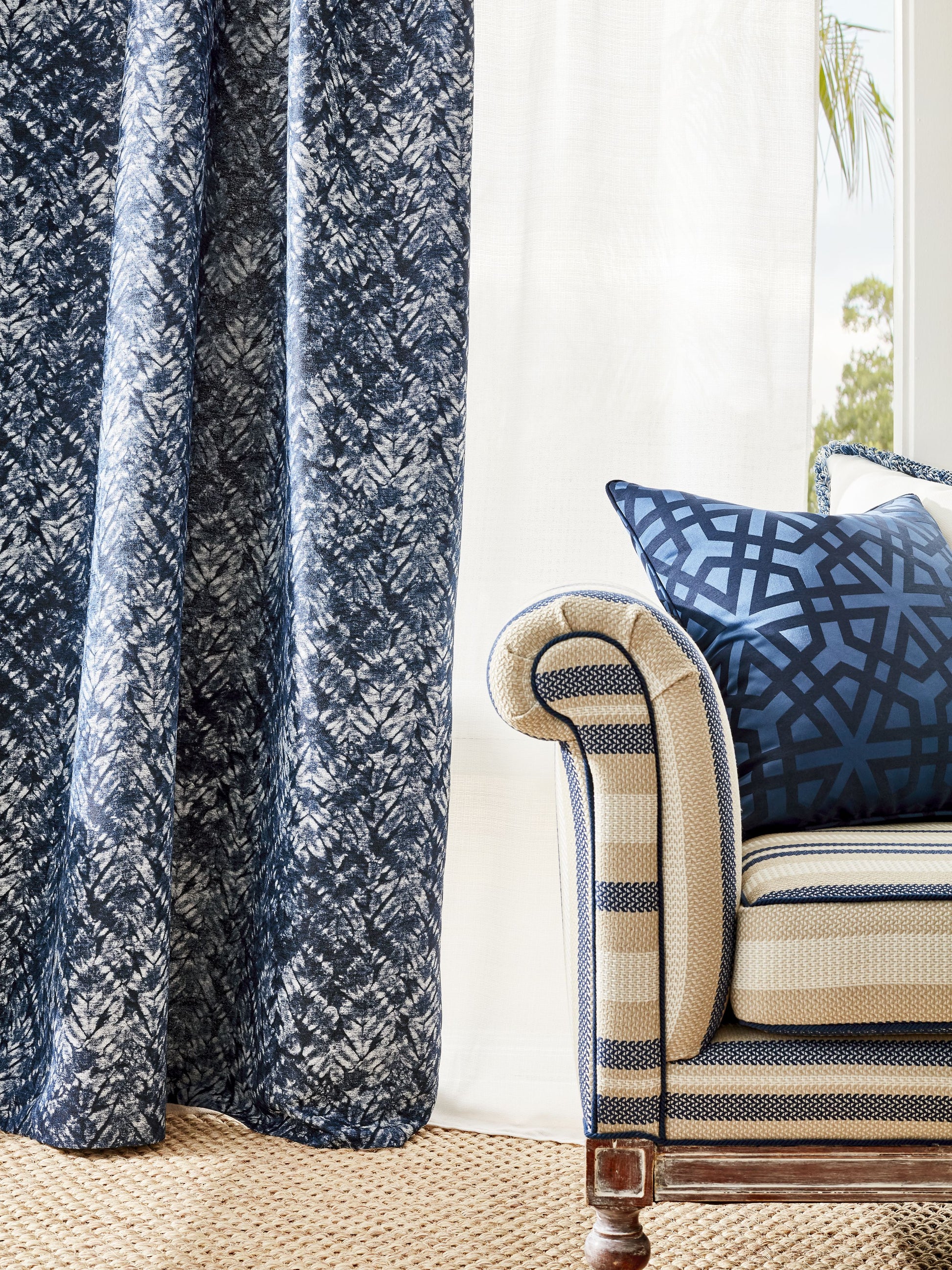 Dark blue leafy-pattern curtains beside striped beige-navy armchair with blue lattice pillow on jute rug.