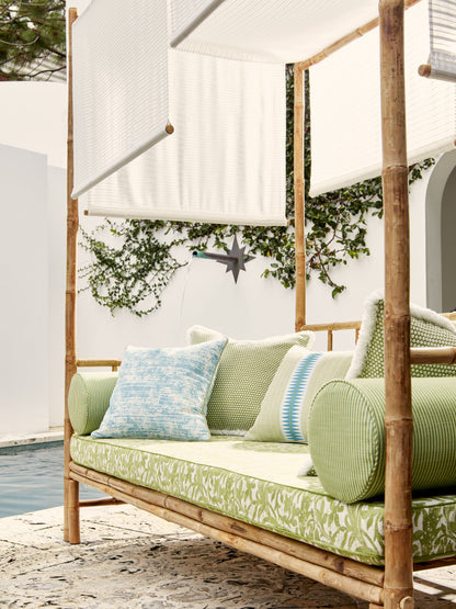 Bamboo outdoor daybed with green patterned cushions and blue pillow under white fabric canopies beside a pool