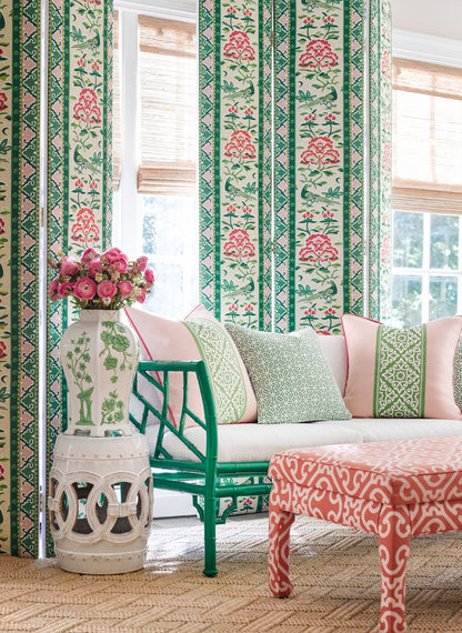 Teal bamboo chair with pink cushions beside floral striped wallpaper, white vase with pink flowers and coral ottoman on jute