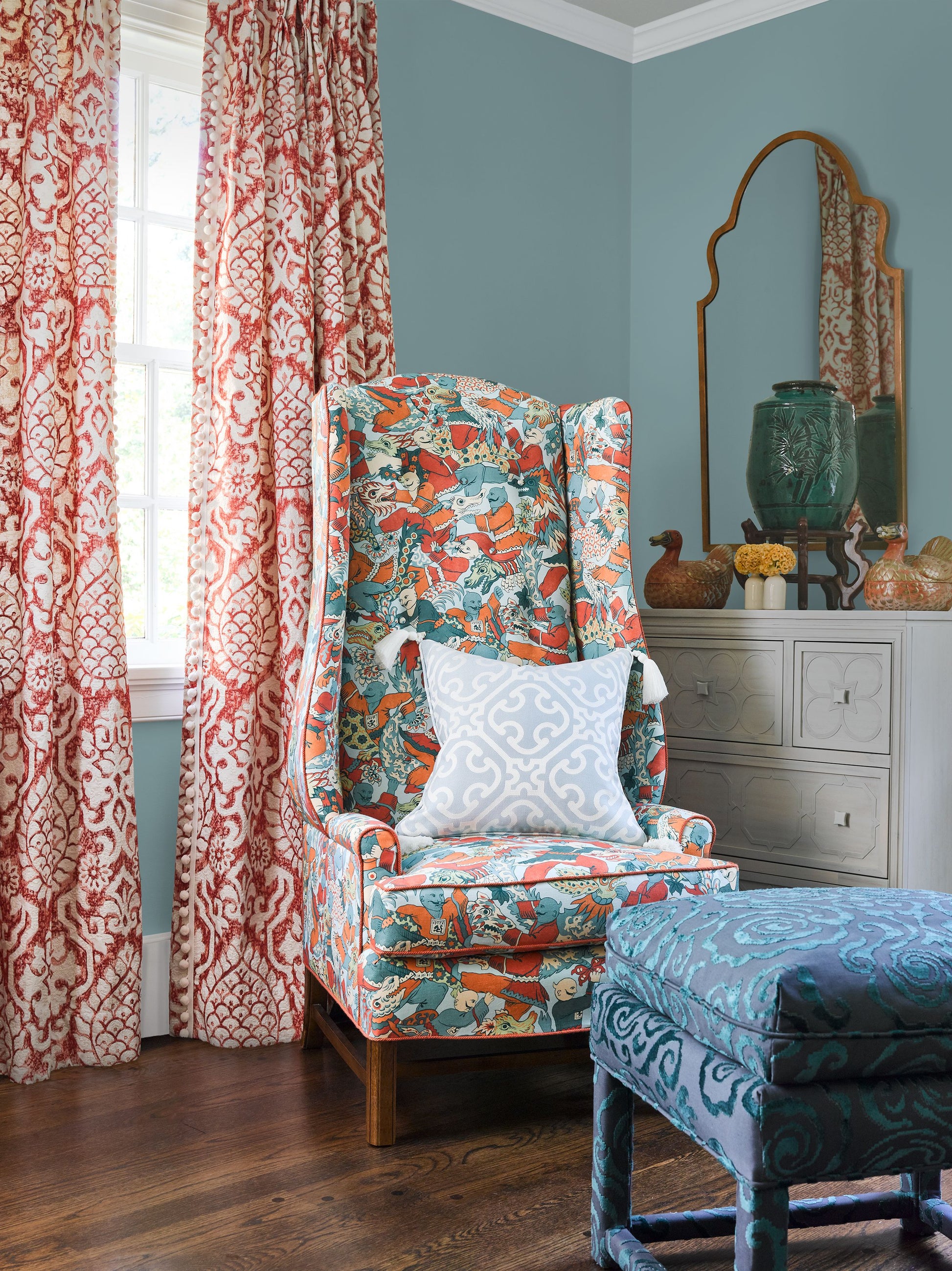 Colorful teal, orange and white patterned wing chair with light blue pillow, paired with a blue patterned ottoman.