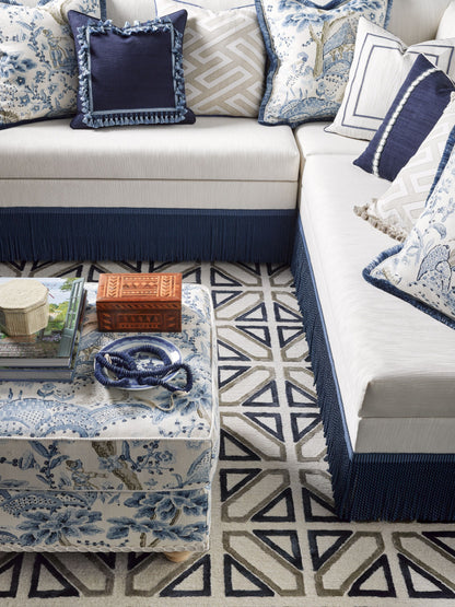 L-shaped beige sectional with navy fringe, blue & white patterned cushions, geometric rug, glass coffee table with blue decor