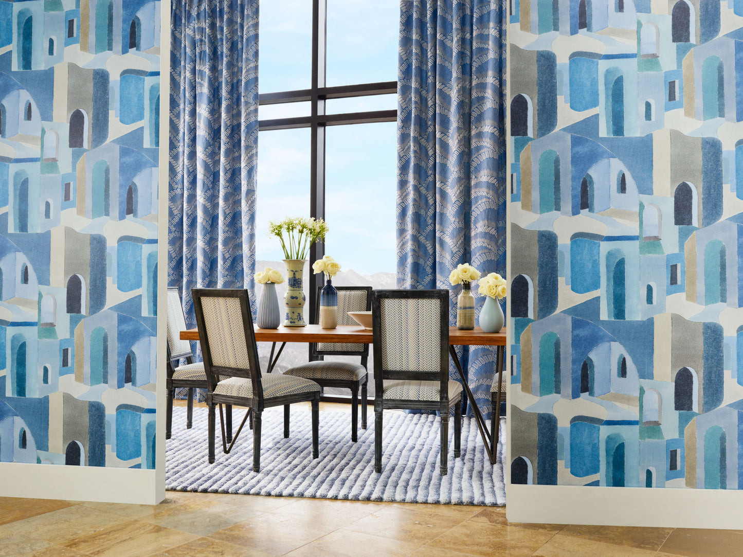 Blue geometric embroidery fabric featuring arches; a dining table and chairs, blue curtains, a striped rug, and yellow flowers are visible.