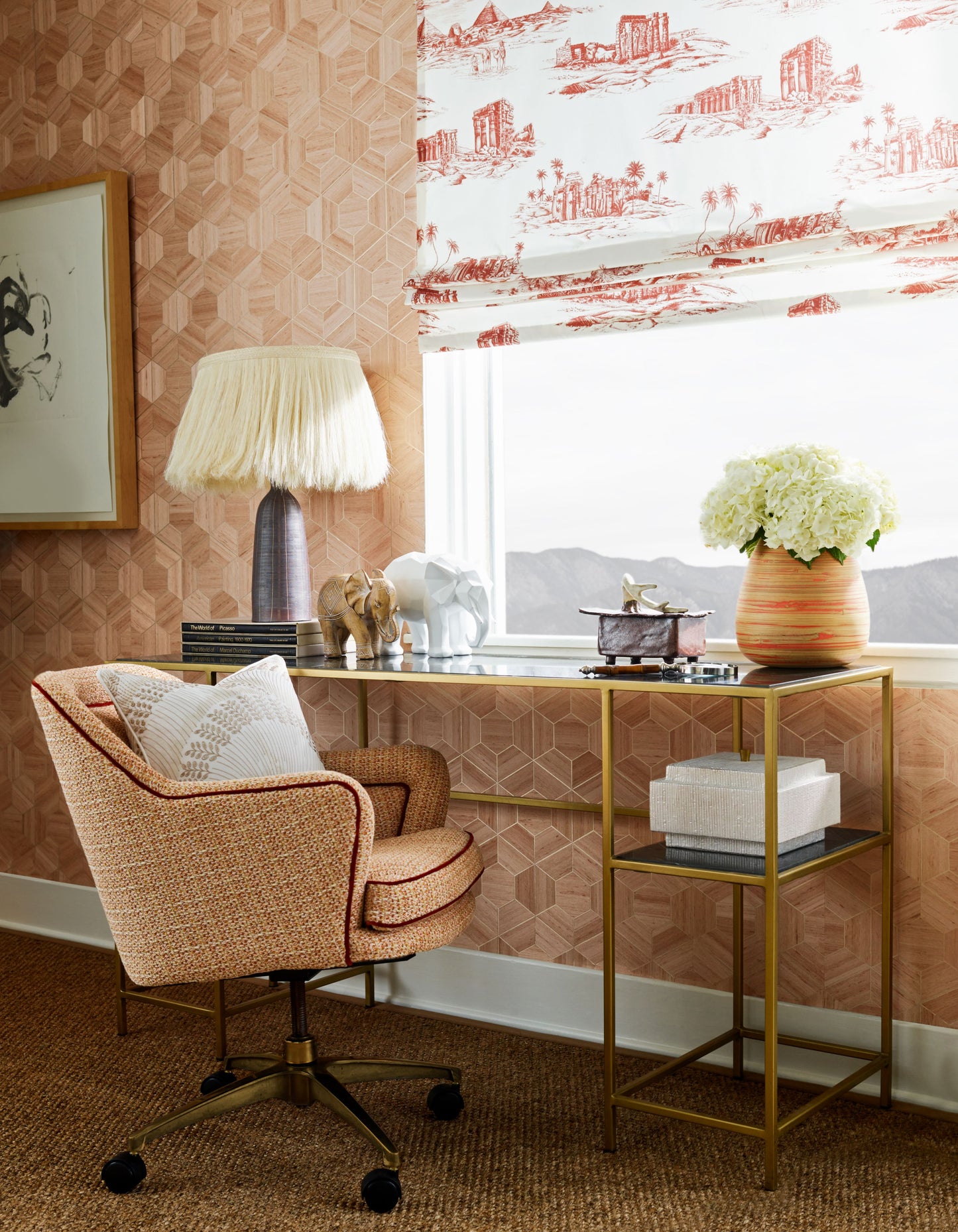 Peach woven swivel chair with cushions beside a gold-tone glass-top console; pink wallpaper, fringed lamp, elephant figurines, white hydrangea vase.