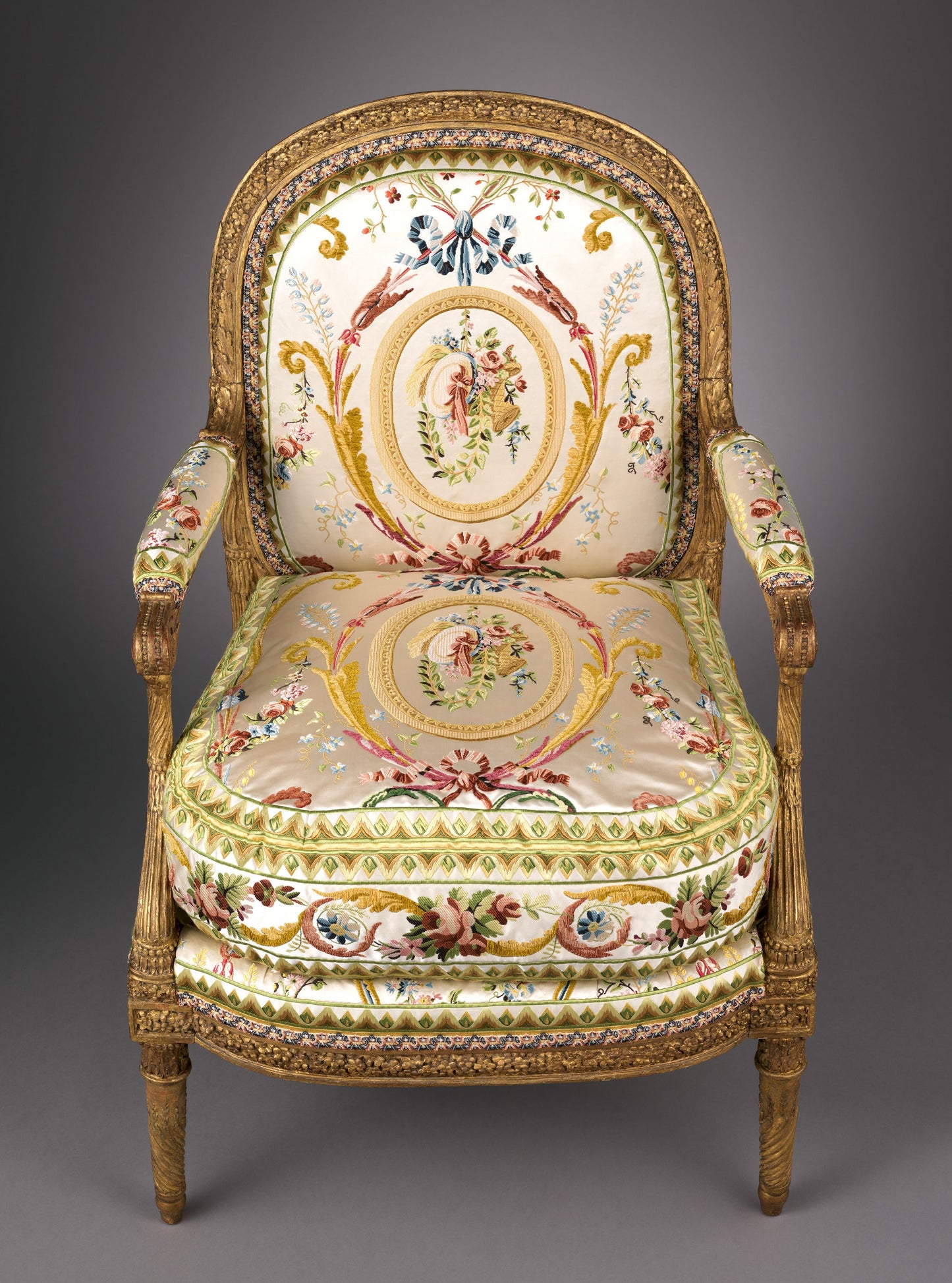 Ornate gilded wood armchair with carved frame and cream silk upholstery featuring floral medallions and scrollwork.