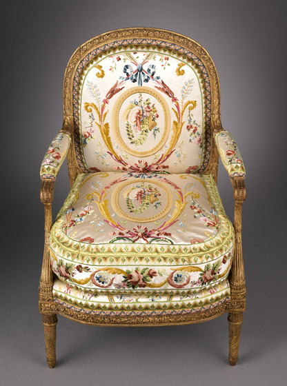 Ornate gilded wood armchair with carved frame and cream silk upholstery featuring floral medallions and scrollwork.