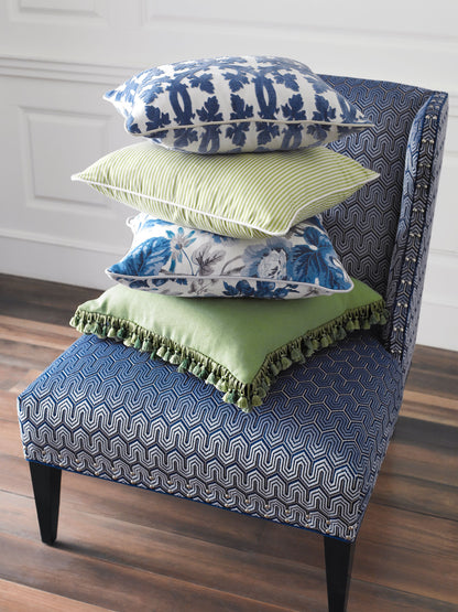 Stacked throw pillows on a blue zigzag chair: white-blue floral, lime striped, blue floral, sage green cushion with fringe.