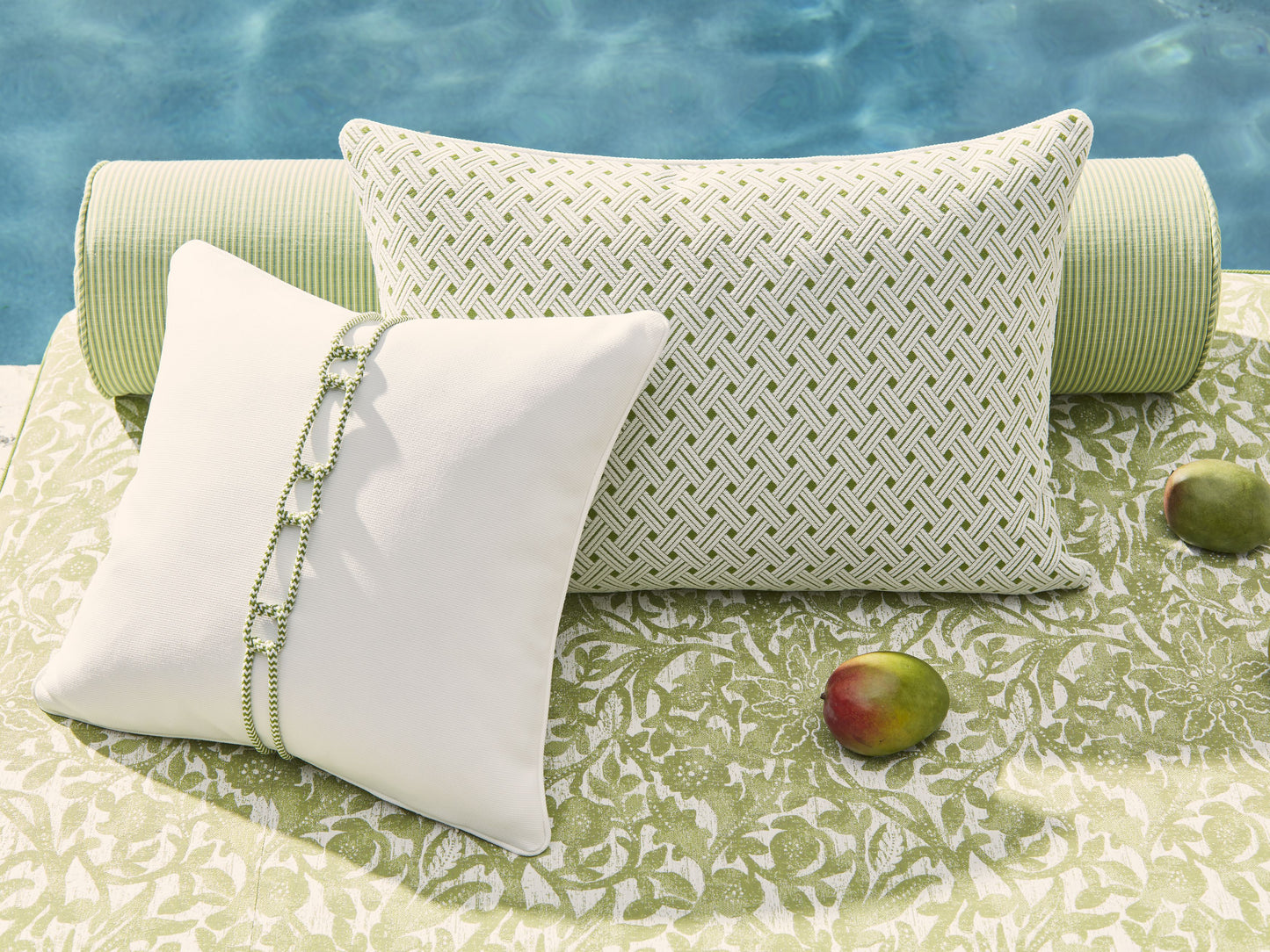 Outdoor cushions: white rectangular pillow with green braided trim, green lattice-pattern pillow, green striped bolster by pool.