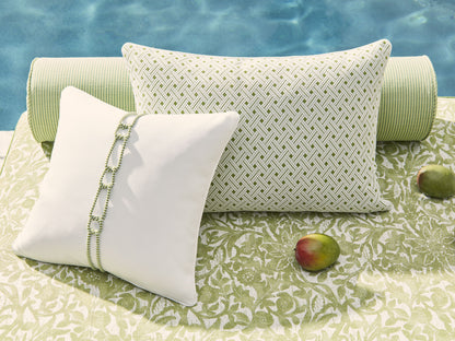 White pillow with green chain trim beside a lattice-green outdoor cushion on a green patterned mat by the pool and mangoes.
