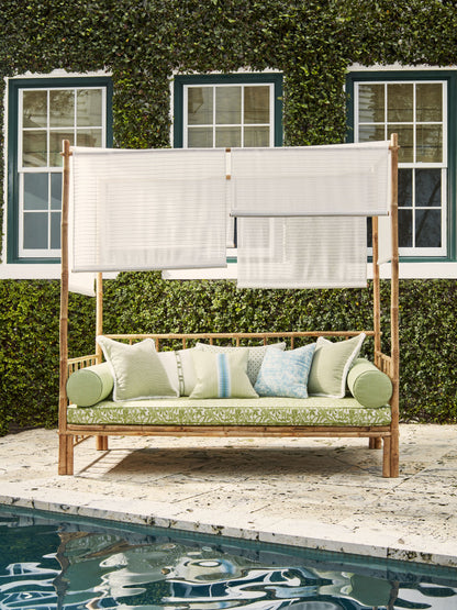 Outdoor wooden daybed with white fabric canopy and cushions, poolside with green cushions and pastel pillows, ivy-covered wall.