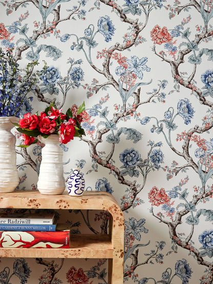 Floral wallpaper with blue, red and brown vines; wooden shelf with ceramic vases and red flowers, plus books below.
