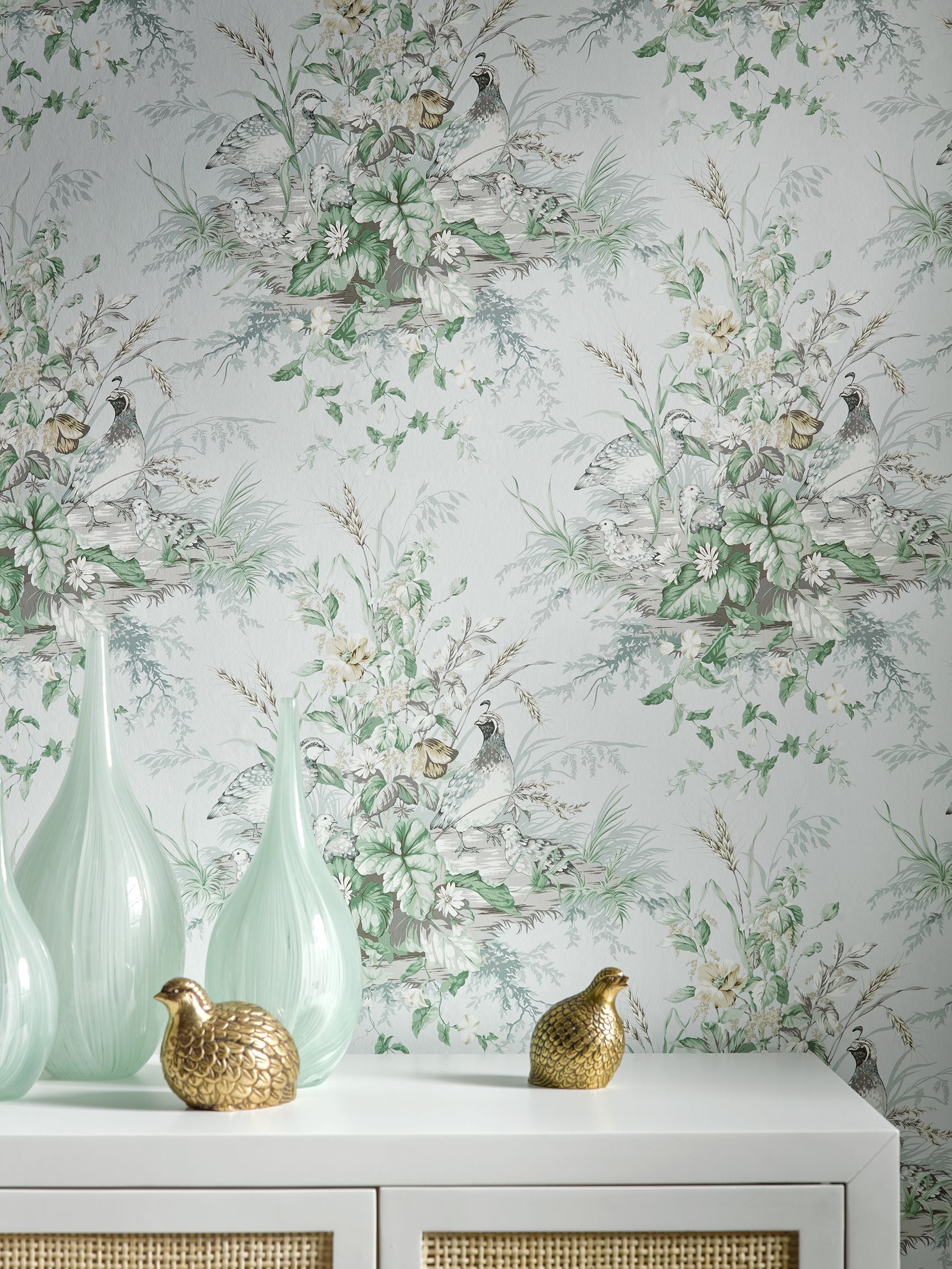 Soft mint-green glass vases on a white console with two gold duck figurines; botanical wallpaper with birds.