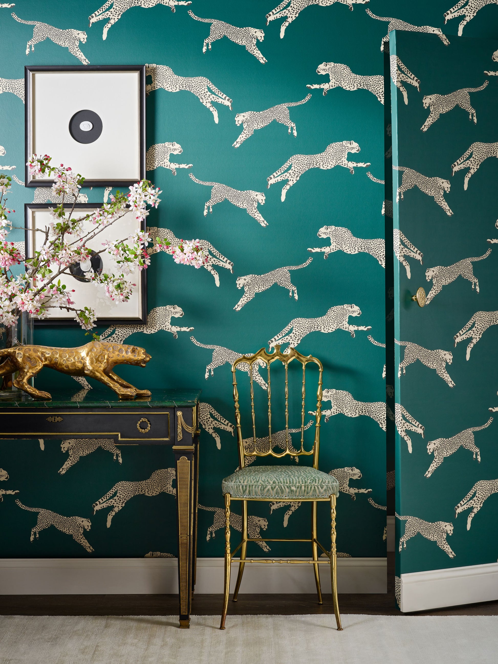 Teal wallpaper with metallic silver cheetah silhouettes; gold console table with framed art and a gold chair.