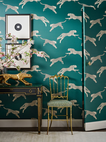 Teal wallpaper with metallic silver cheetah silhouettes; gold console table with framed art and a gold chair.