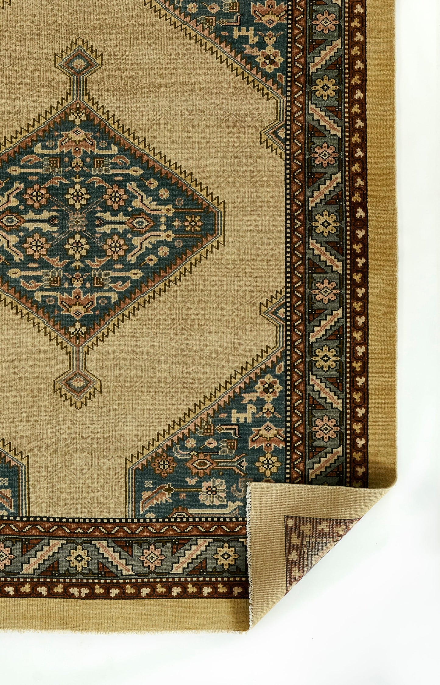 Beige oriental rug with teal central medallions, brown floral border, ornate geometric motifs; folded corner.