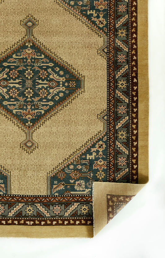 Beige oriental rug with teal blue diamond medallion, floral border; Persian-inspired pattern, corner folded.