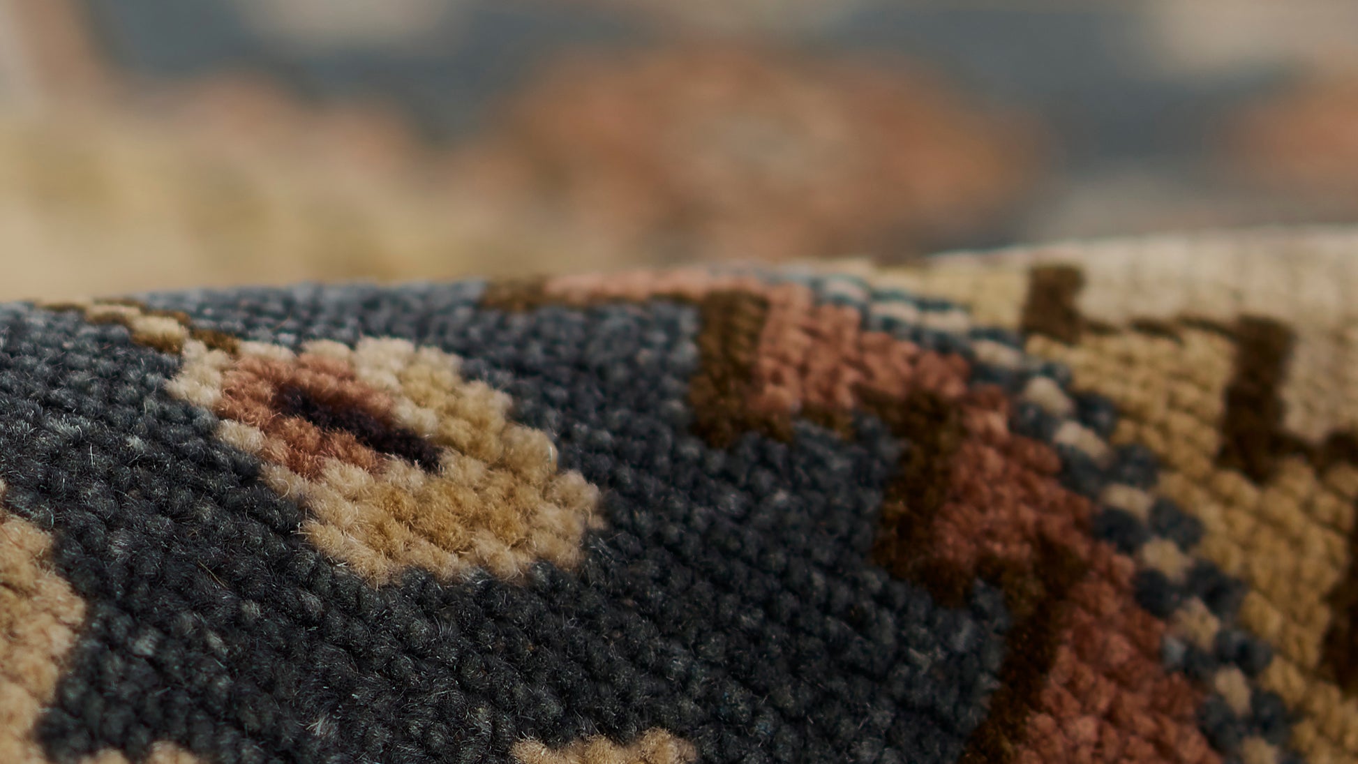 Close-up of a navy blue woven rug with beige, tan and rust geometric motifs and plush pile.