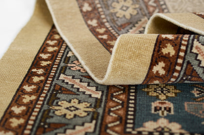 Beige and brown Persian-style rug with teal accents, geometric borders, and woven texture; rolled edge visible.