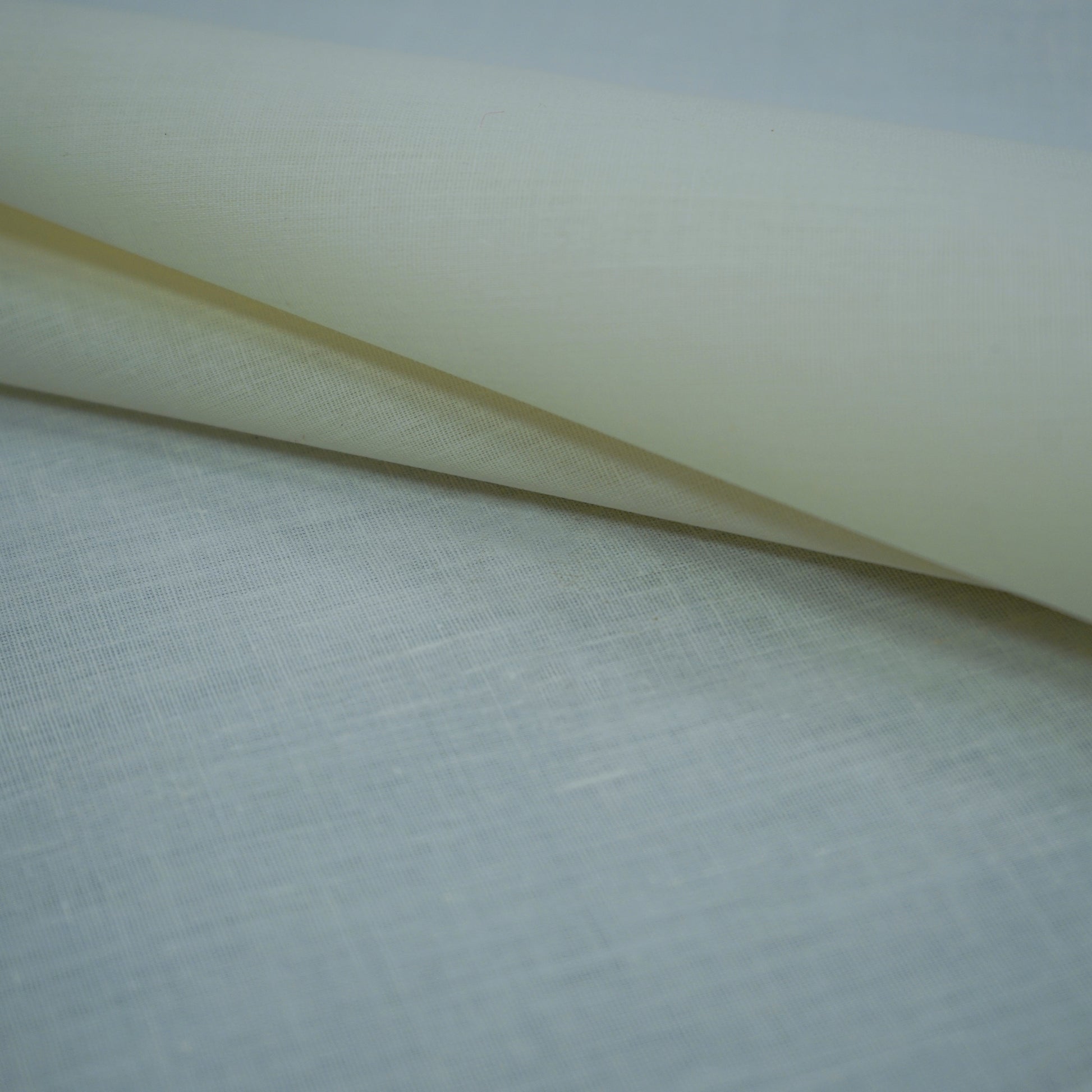 Cream offwhite plain lining fabric roll with a natural woven texture, draped on a pale blue backdrop.