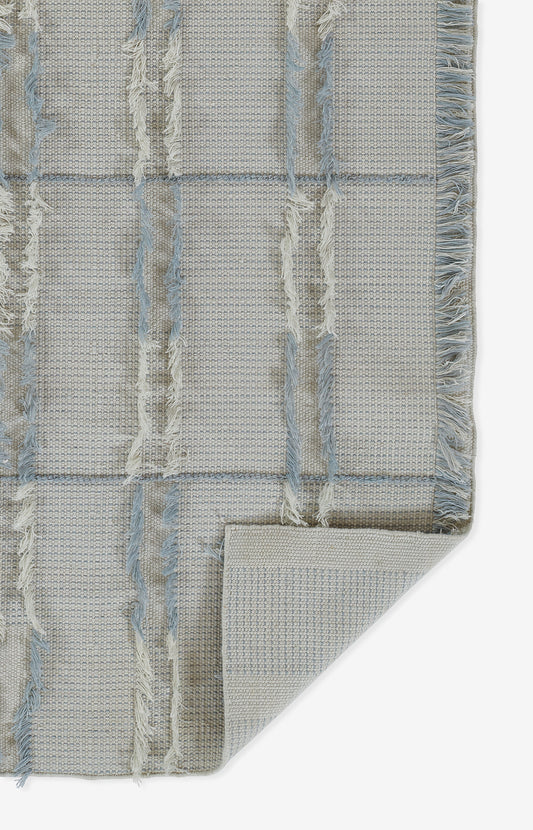 Beige and pale blue flat-weave rug with a grid pattern, fringe tassels, and a folded corner.