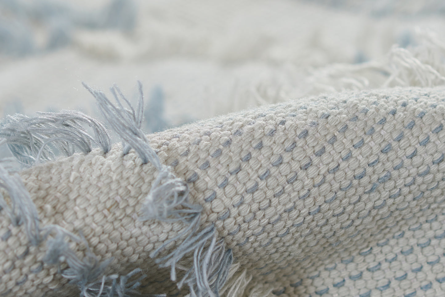 Close-up of a cream and pale blue woven runner rug with fringe tassels and a textured dotted pattern.